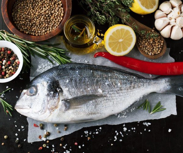 Bar de ligne entier prêt à être cuisiné entouré de ses aromates, servant pour le plat intitulé Le Loup de Wall Street du restaurant La Table de Trois à Bordeaux